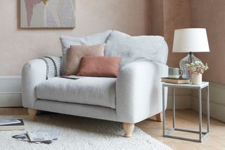 A pale gray Loaf love seat in the corner of a neutral living room, with pale pink accents.