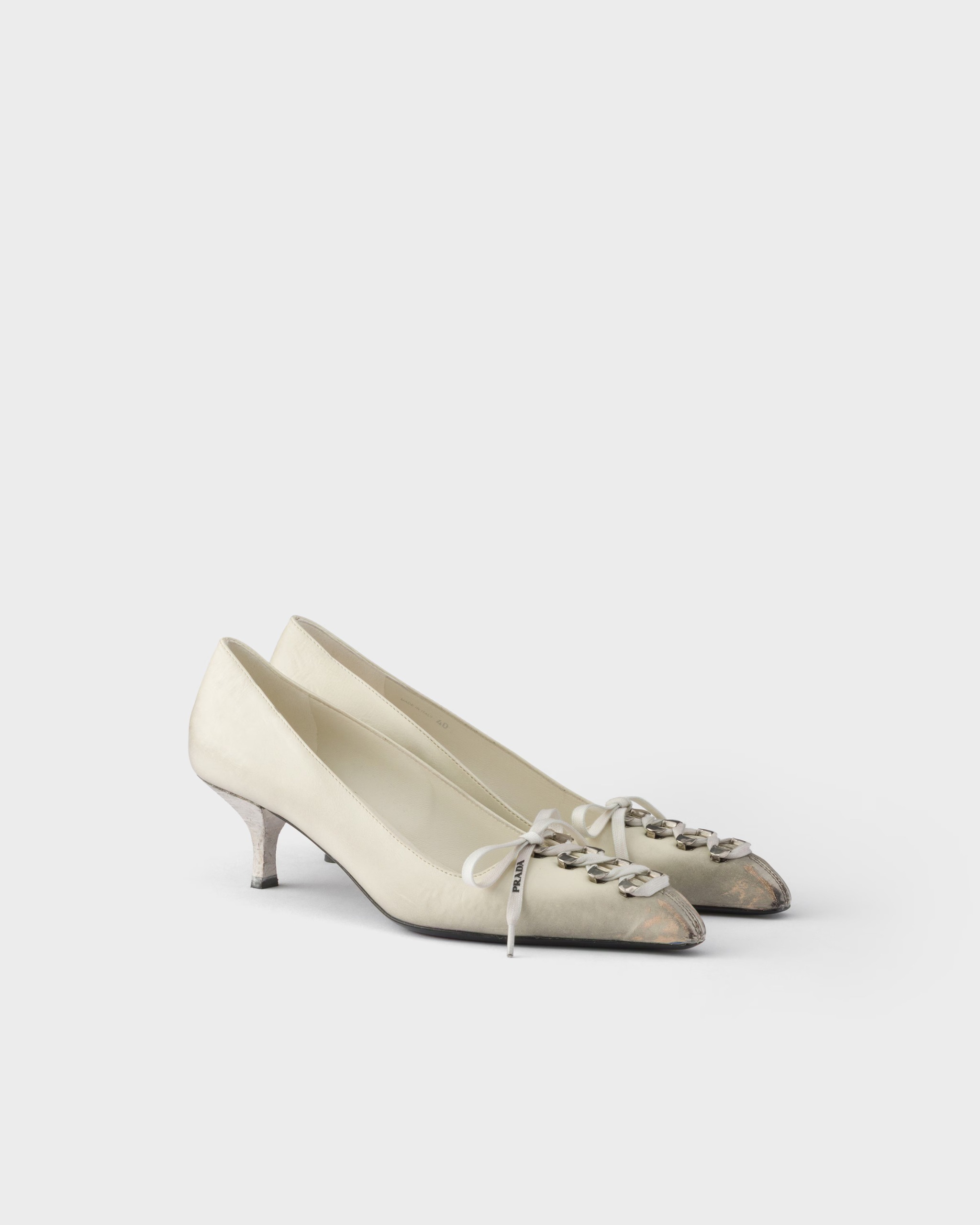 An image of antique-looking white kitten-heel pumps with laces on the toes from Prada