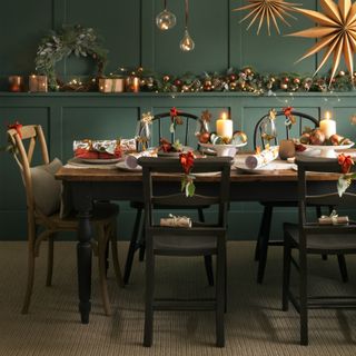 A green dining room decorated for Christmas with large stars hanging from the ceiling and the table set for Christmas dinner