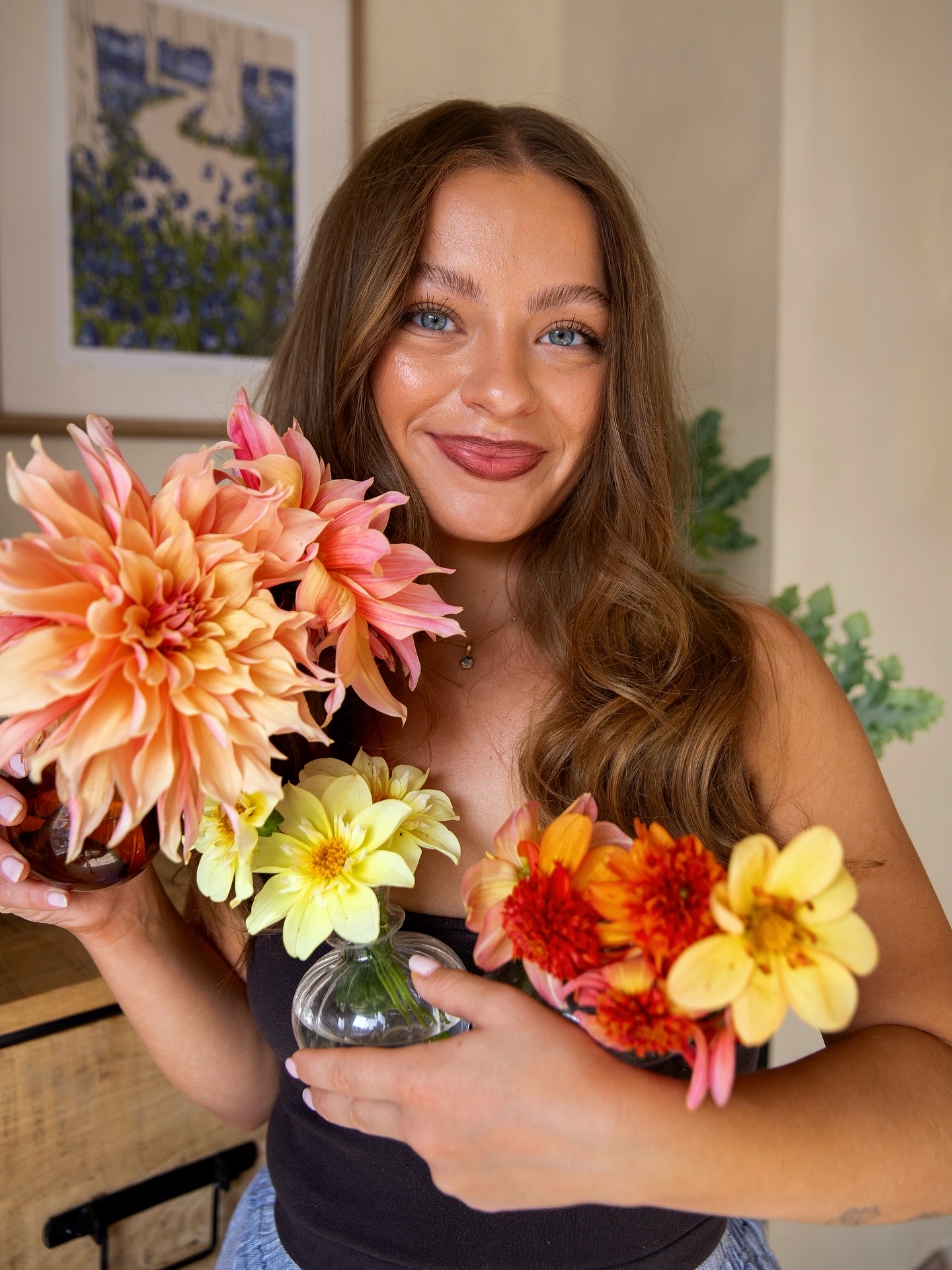 brunette woman smiles to camera holding vases of dahlias