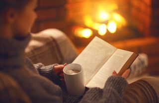 A woman enjoying a book in front of the fire with a mug of hot chocolate.