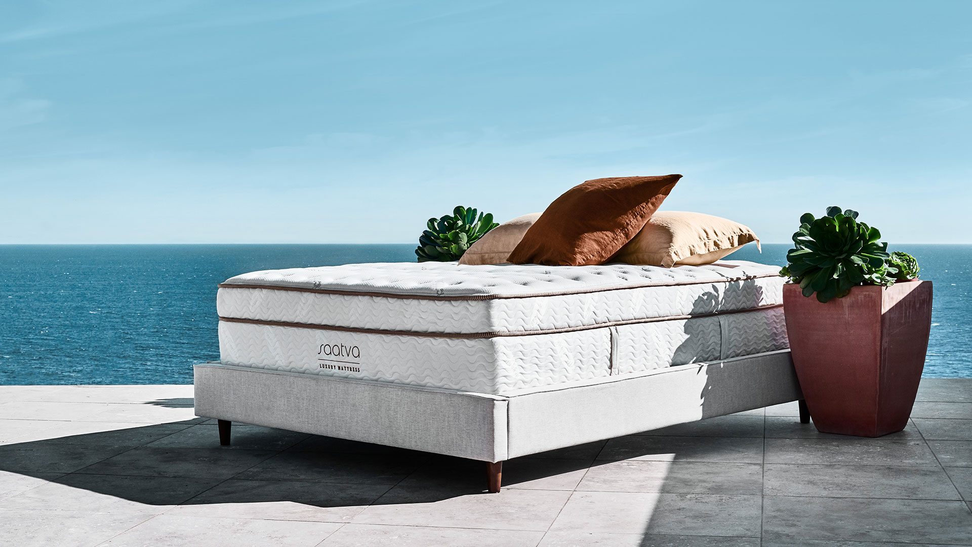 Click image of the Saatva Classic mattress, our top mattress pick, on a sunny patio area with the sea in the background