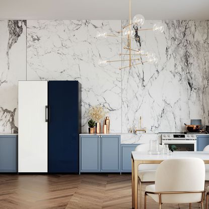 A Samsung black and white fridge freezer in a kitchen with marble effect wallpaper and brass lighting
