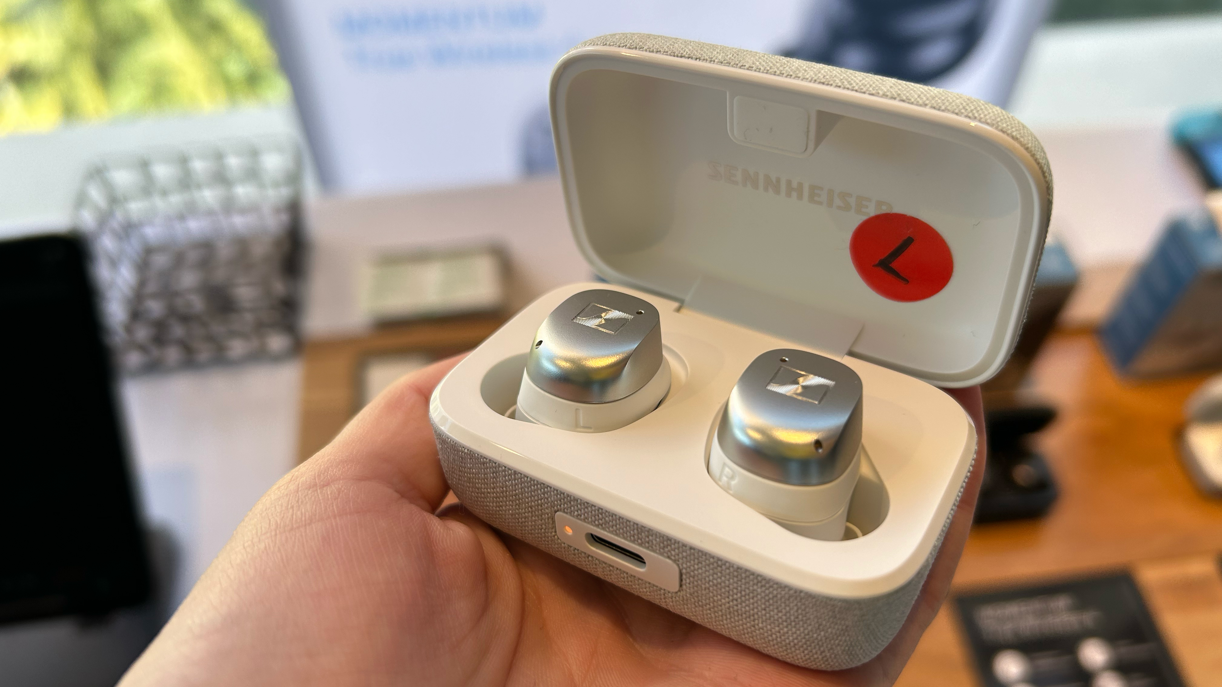 Sennheiser Momentum 4 true wireless earbuds in their case, held in a hand at a trade show