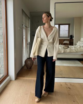 woman wearing cream knit wrap top, cream tote bag, wide leg blue denim, beige Chanel shoes