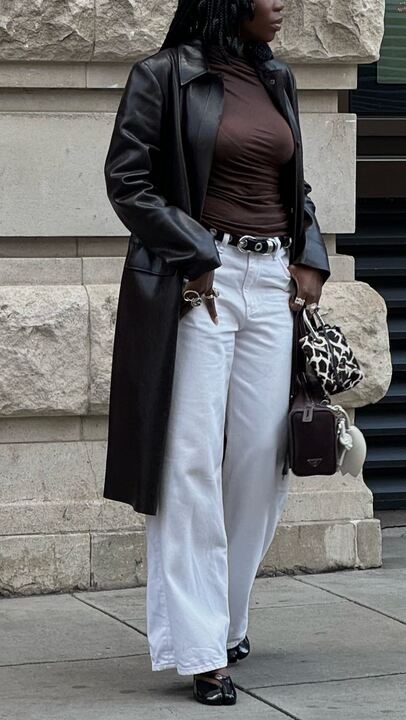 Influencer @daniellejinadu wears white jeans with black flats and a black leather coat. She carried a cow-print bag and wears a studded belt.