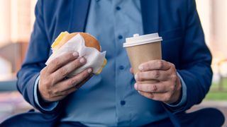 Overweight man holding hamburger and coffee