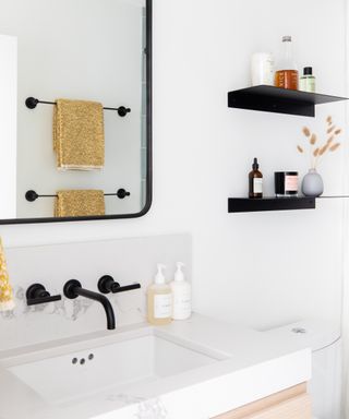 A white bathroom with white circular wall tiles, black framed mirror and black faucet