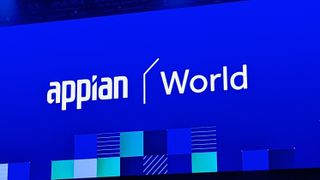The Appian logo (stylised text reading 'appian') next to the word 'World' in white on a large blue led screen, shot from a distance on a conference stage