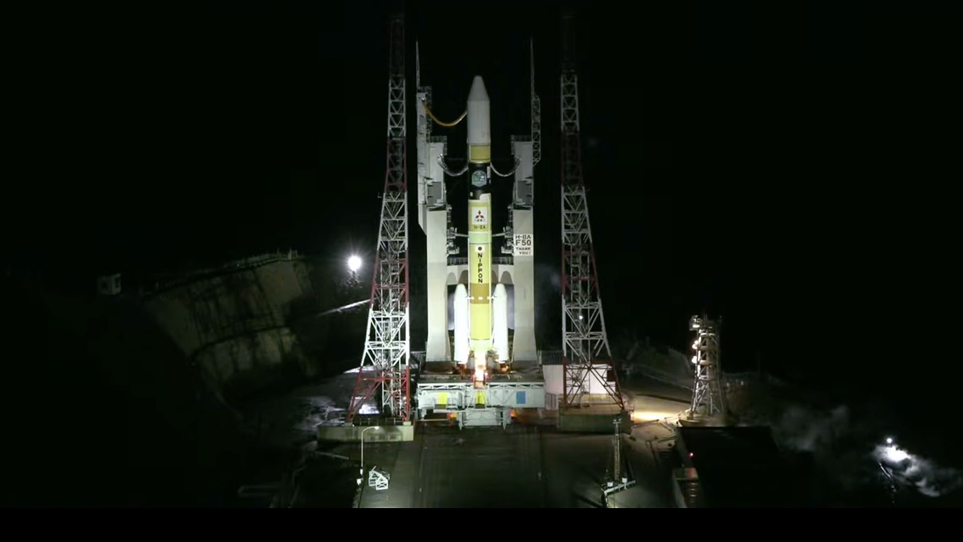 an orange and white rocket ignites its engines on the launch pad for a night liftoff