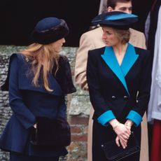 Sarah Ferguson and Princess Diana talking to each other wearing blue suits and hats