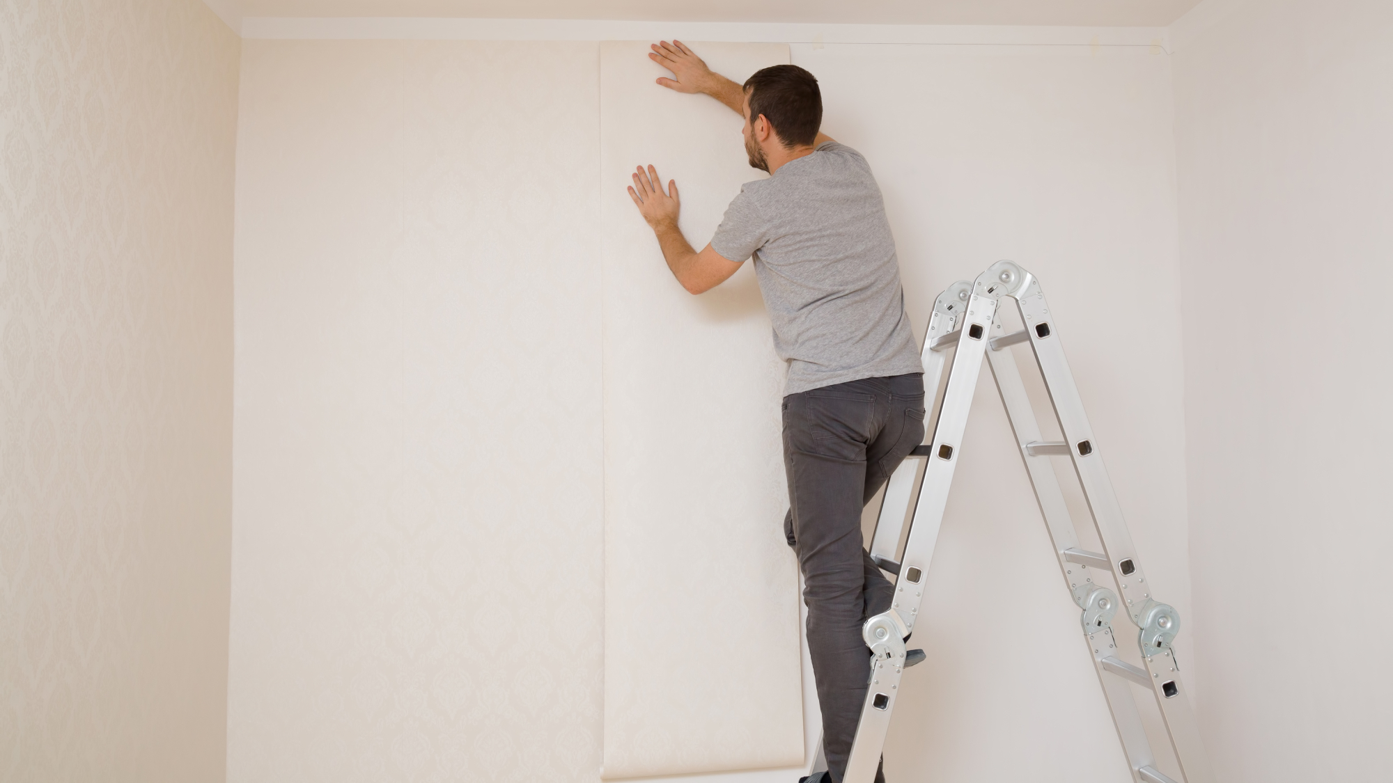 man stood on ladder hanging wallpaper on walls