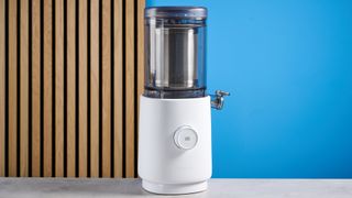 the nama m1 plant-based milk maker in white with a pitcher, blade frame, and strainer, and a pulp mat accessory with a brush