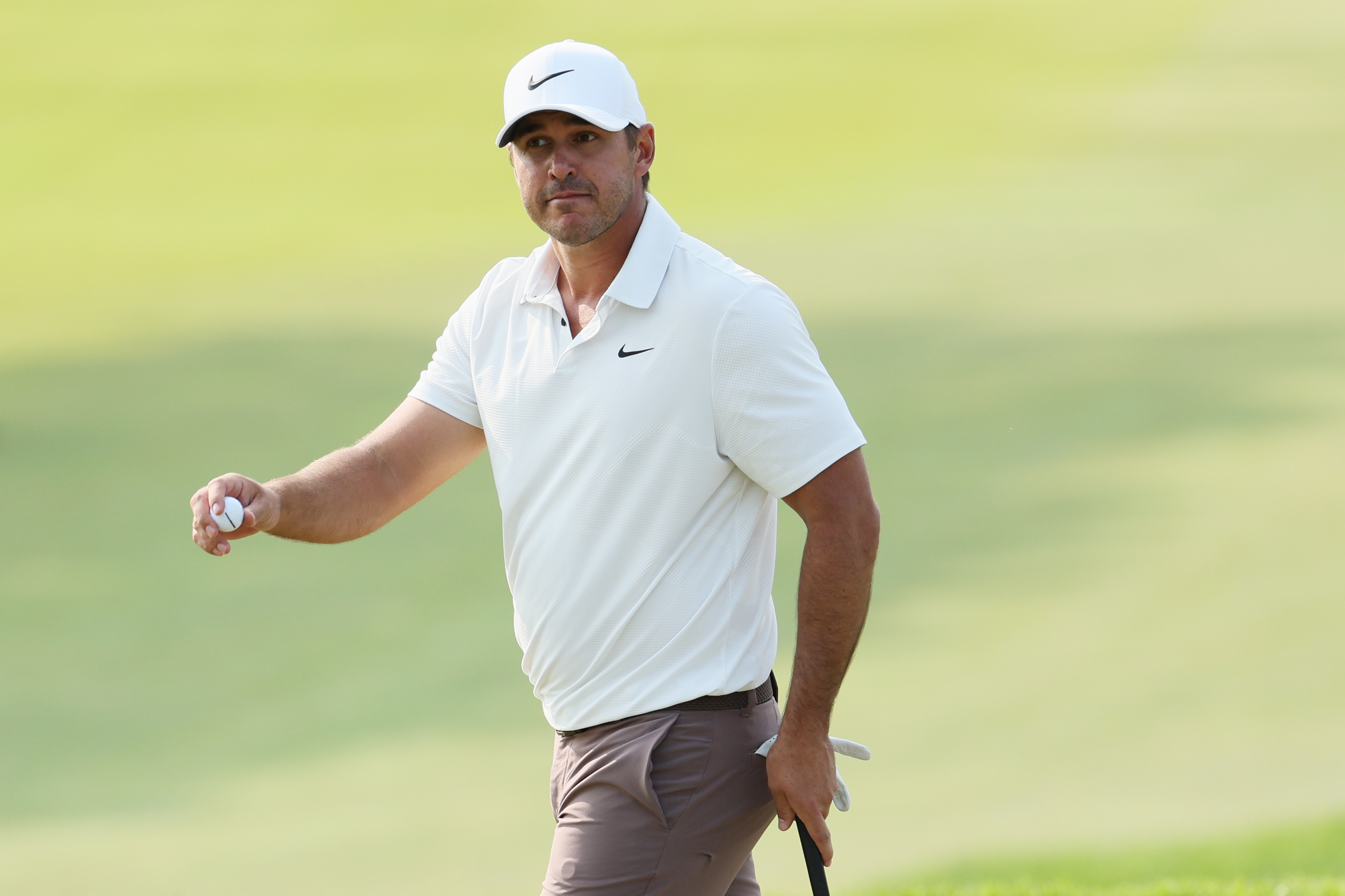 Brooks Koepka walks off the green holding a golf ball