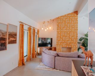 Honey hued floor length drapes and color-match patterned feature wall, with gray curved sofa.