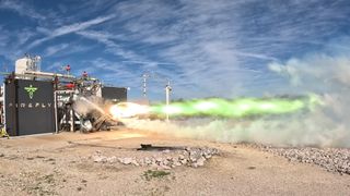 a rocket engine mounted on a test stand in the desert blasts out a plume of green flames