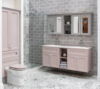 Bathroom with double vanity in pink with gray wall cabinets above, cabinet above WC, shower, patterned floor tile and gray tile floor