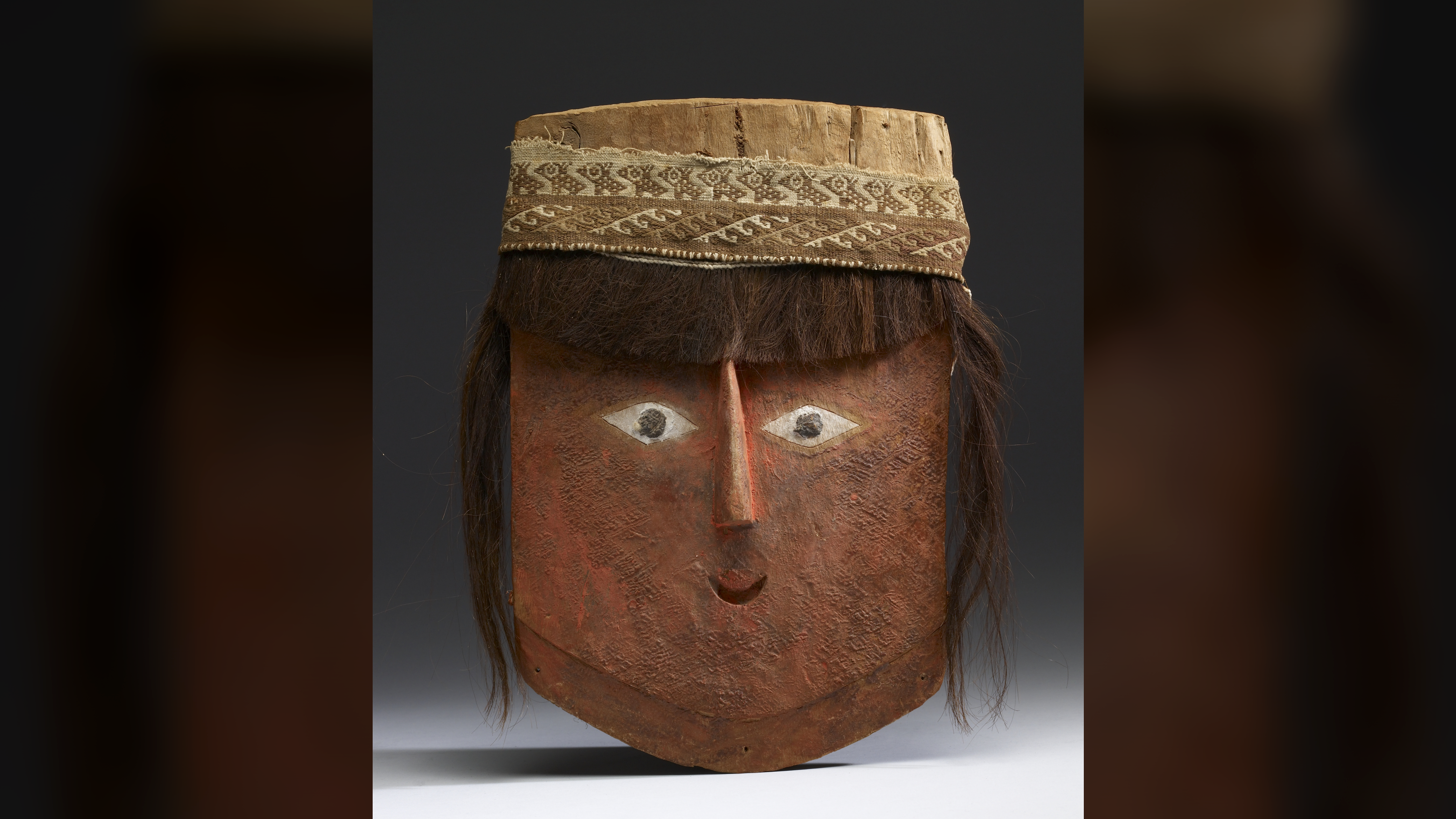 a red-painted wooden mask in the shape of a stylized human face with human hair attached