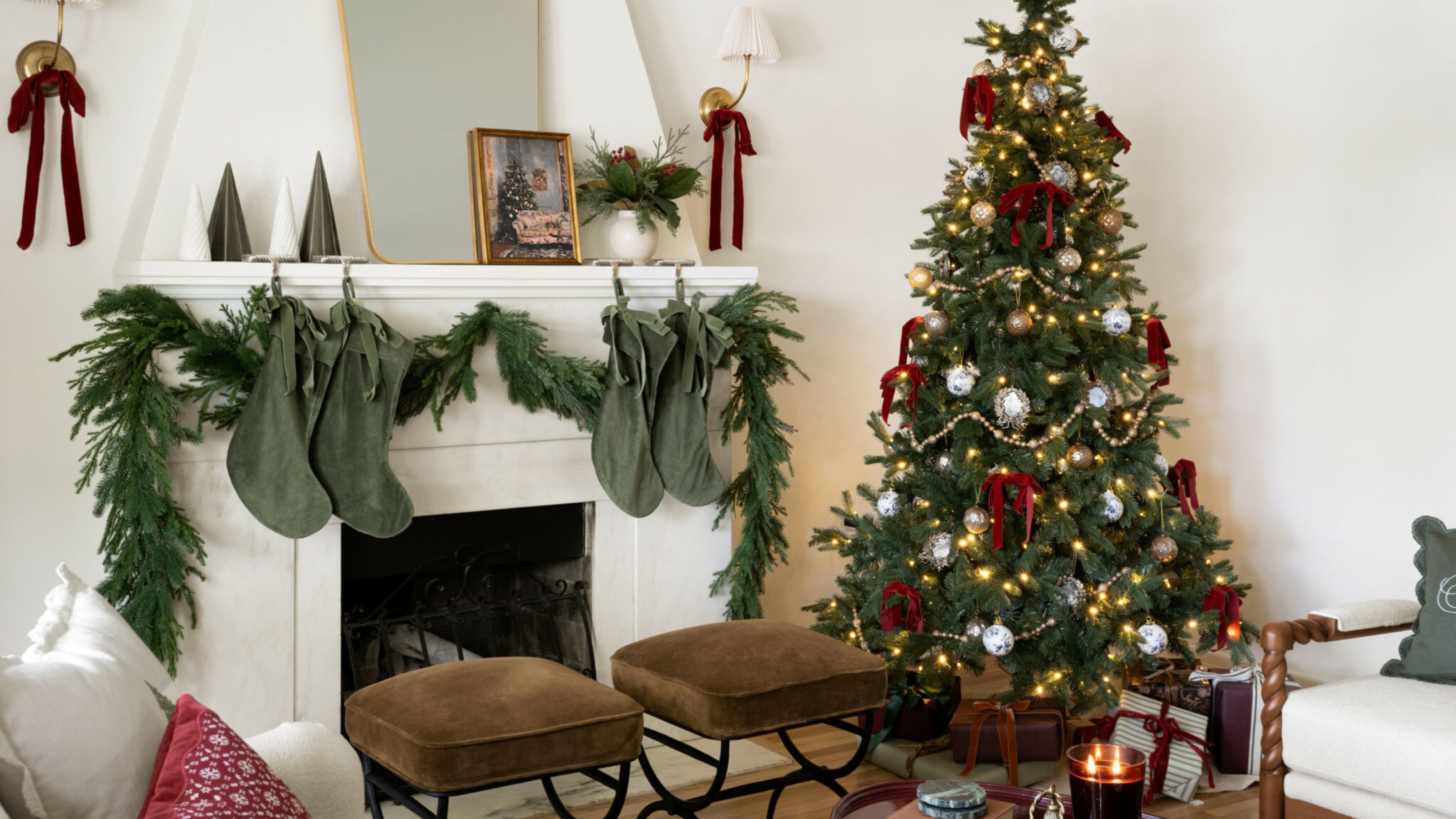 White living room with a fireplace decorated for the holidays with a tree in red and gold and an evergreen garland with green velvet stockings