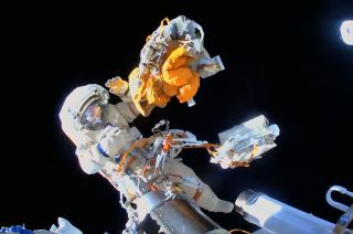 cosmonaut in a white spacesuit lets go of a yellow bundle of spent equipment while on a spacewalk outside the international space station