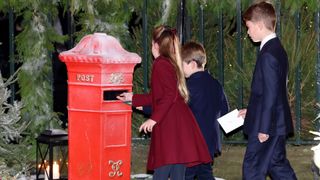 Princess Charlotte, Prince George and Prince Louis putting letters into a red mailbox next to a snowy tree