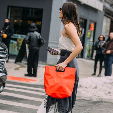 woman wears tank top black scarf and white skirt with red handbag