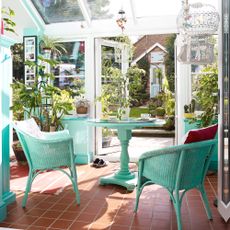 A terracotta tiled floor in a conservatory with green wicker table and chairs