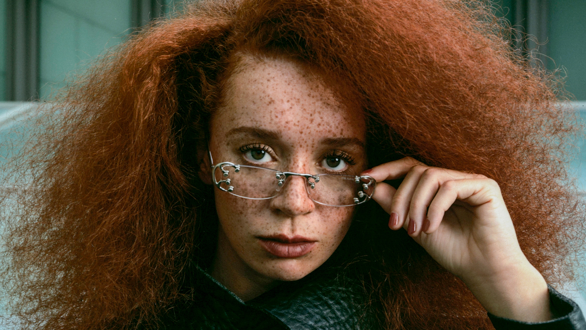 Hero image for Erin Kellyman Ones to Watch story. She is pictured wearing a Prada jacket and metal-accented glasses.