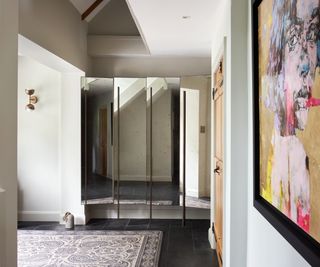 hallway with black floor tiles and large mirrored bespoke storage built into alcove, bright artwork on wall and patterned rug on floor