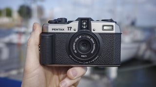 Pentax 17 compact film camera front-on, in the hand with boats in background