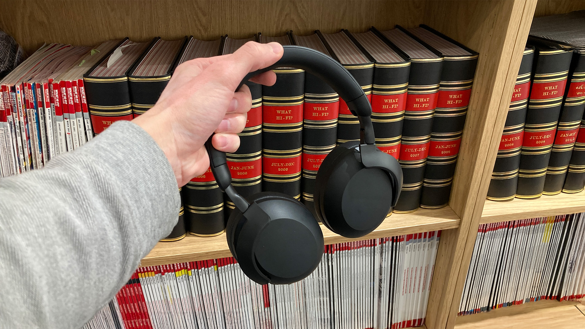 Philips TAH8000E wireless over-ear headphones held in hand in front of bookcase