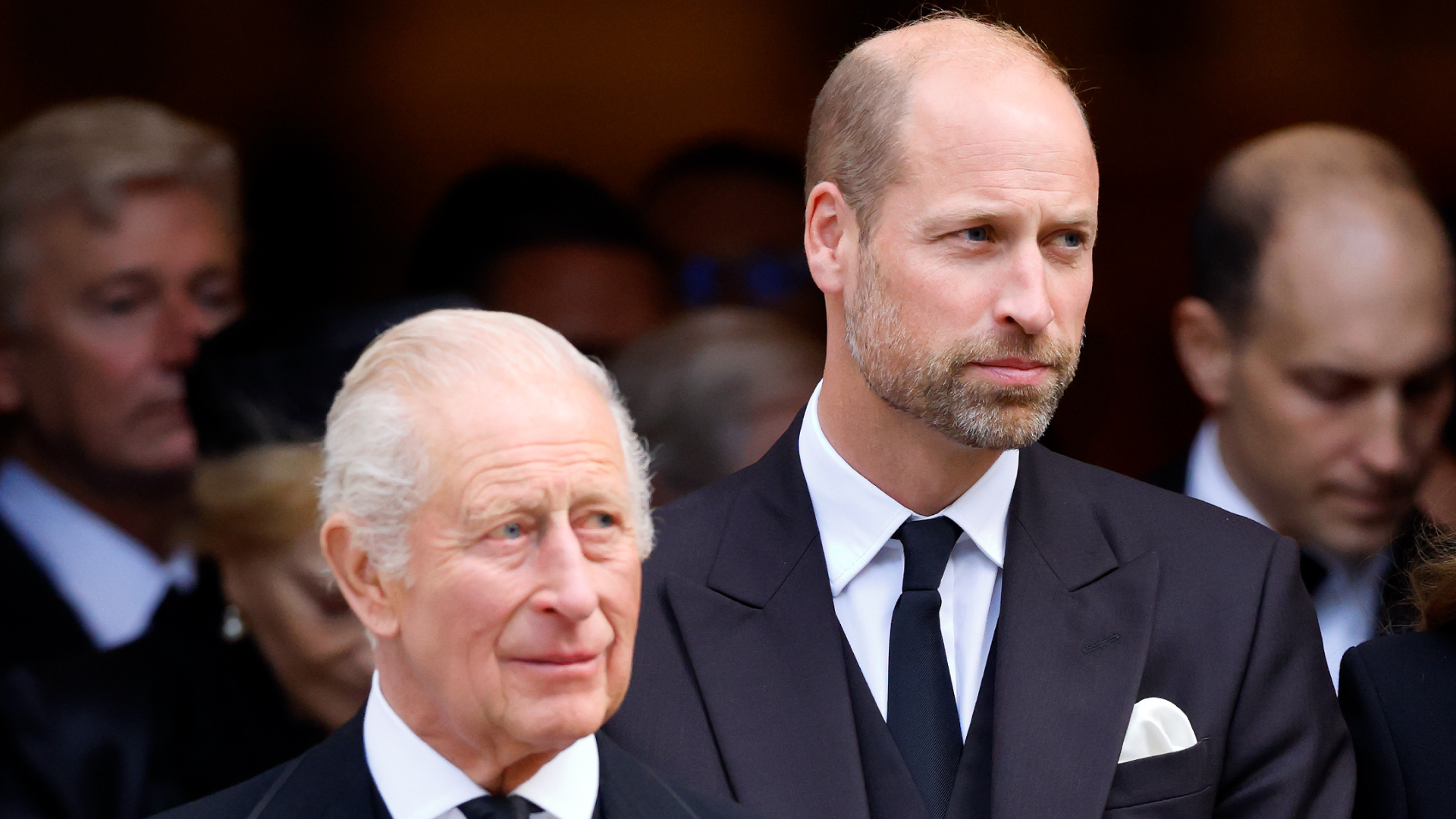 King Charles and Prince William wearing black suits and ties standing next to each other