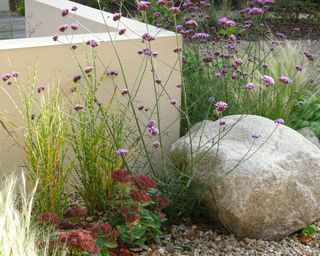 large boulder in a flower bed softened with pretty planting and grasses