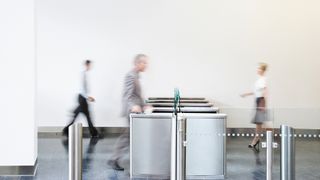 A photo of employees, who are blurry with motion, walking through an office turnstile to represent return to office (RTO) mandates.