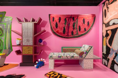 A Memphis Milano-inspired design showcase features bright pink walls and just as striking furniture including reclining sofas, wardrobes, lights, and tables.