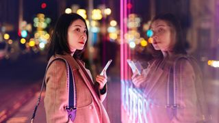 Young woman using mobile phone against neon light display on city street at night