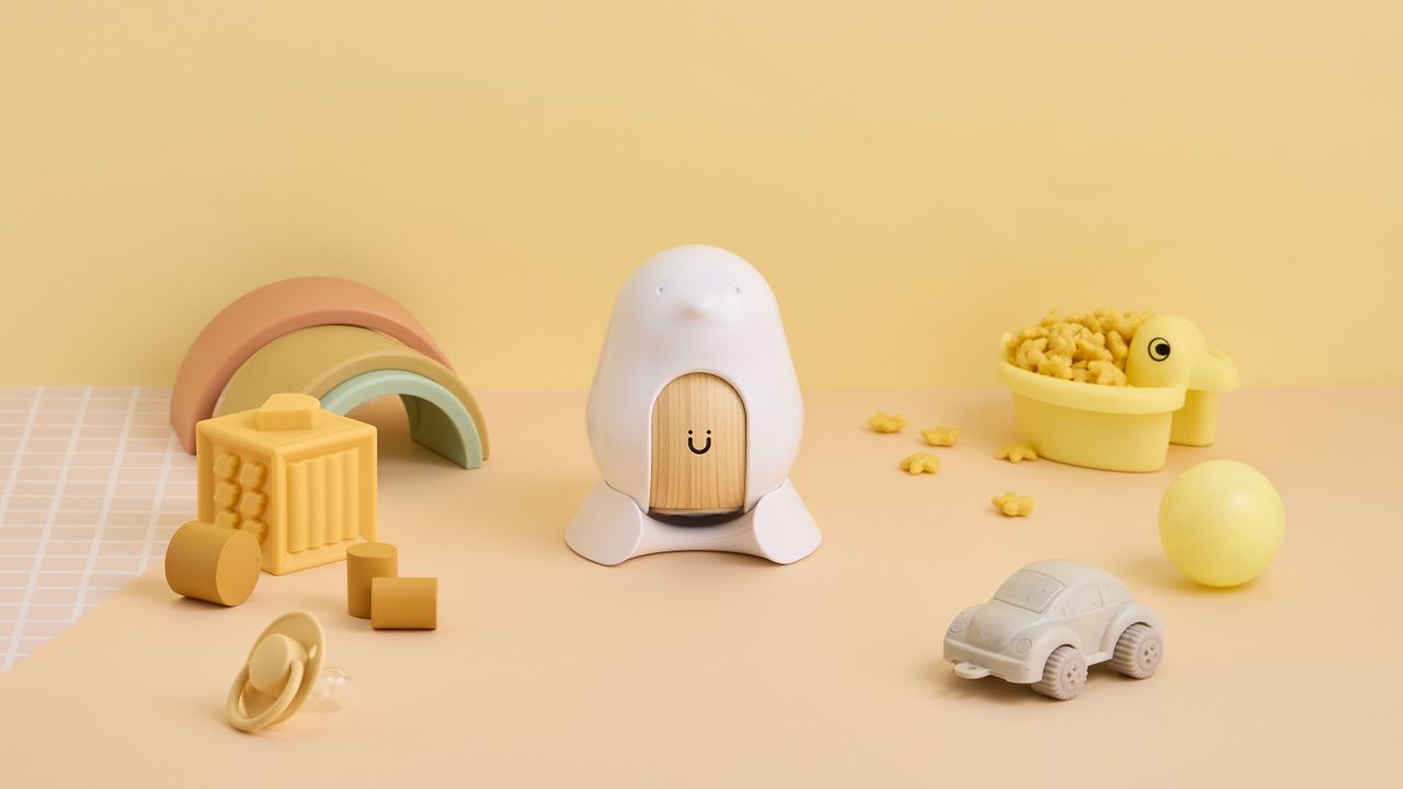 The Cubo Ai Smart Baby Monitor on a yellow background with baby toys