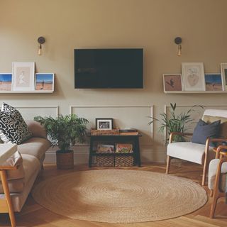 A beige-painted living room with a round jute rug and a wall-mounted TV