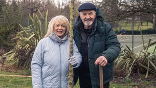 Alison Steadman in a light blue coat holds a tree and stands next to Larry Lamb in a dark hat and jacket in Alison & Larry: Billericay to Barry.
