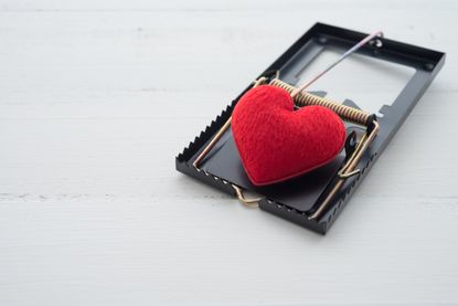 Red heart in a mousetrap on white background, online romance scams concept