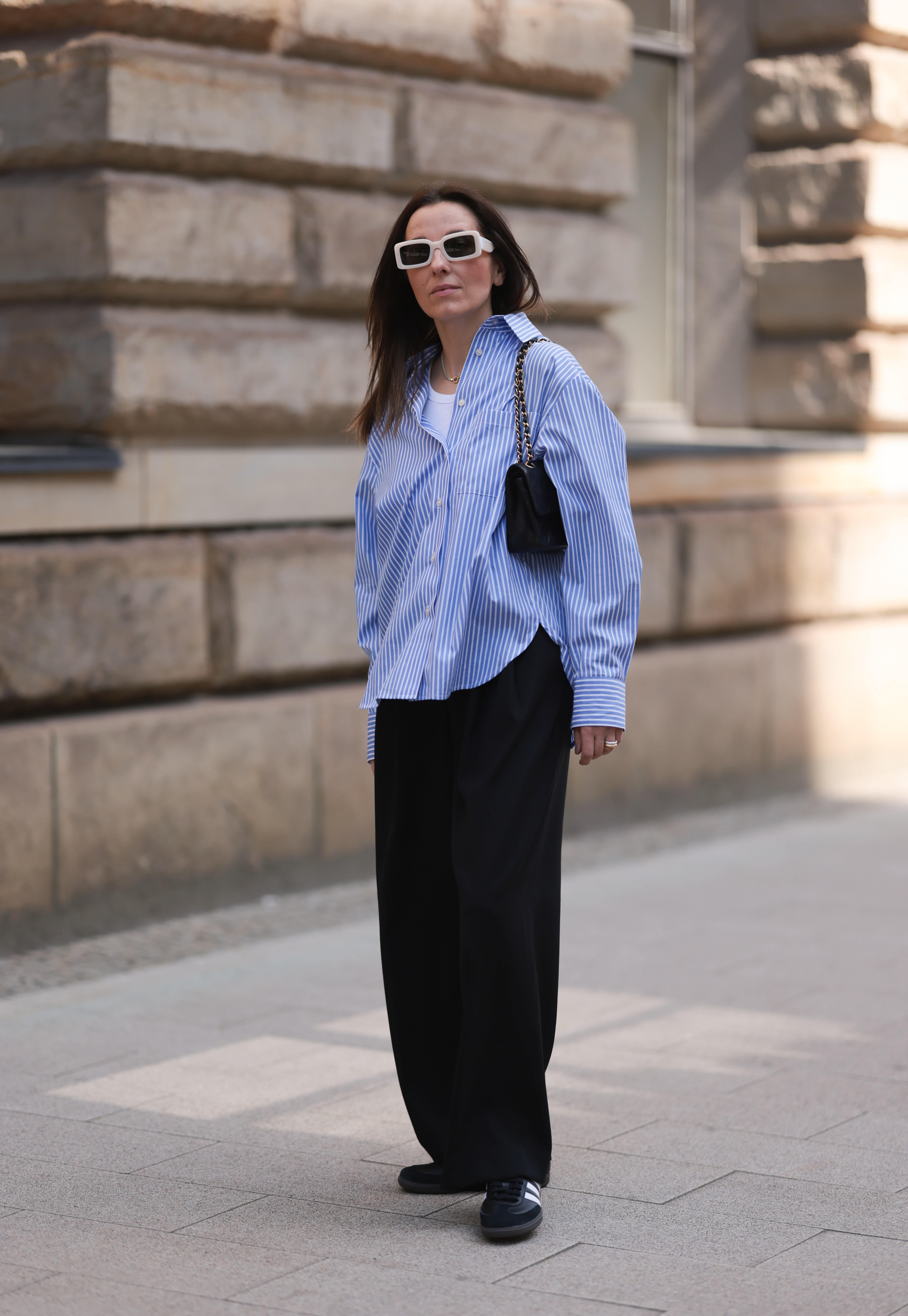 woman wearing blue-and-white button-down shirt, black pants, and black adidas sambas