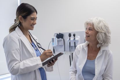A young female medical doctor is meeting with a senior female patient. She is smiling as she is looking at her patient.