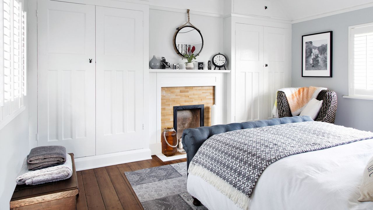 Bedroom with dark wooden floor, built in cupboards either side of the fireplace, pale grey walls and a large double bed with white and black bed covers