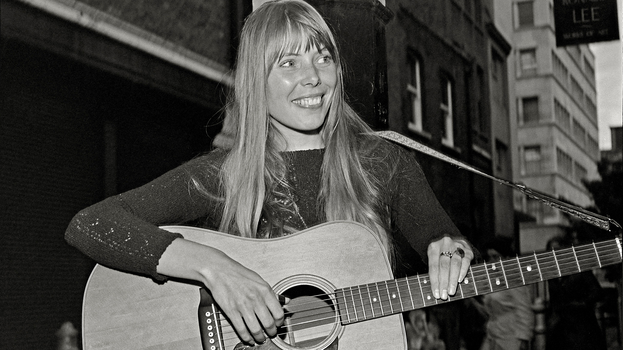 Joni Mitchell strums guitar outside the The Revolution Club, London, England, September 17, 1968. On tour for the release of her debut album Song to a Seagull. Image from 2.25 X 2.25 inch negative.
