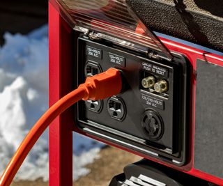 An orange gen-cord plugged into a black and red portable generator outside