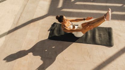 Woman doing Pilates boat pose on a yoga mat.
