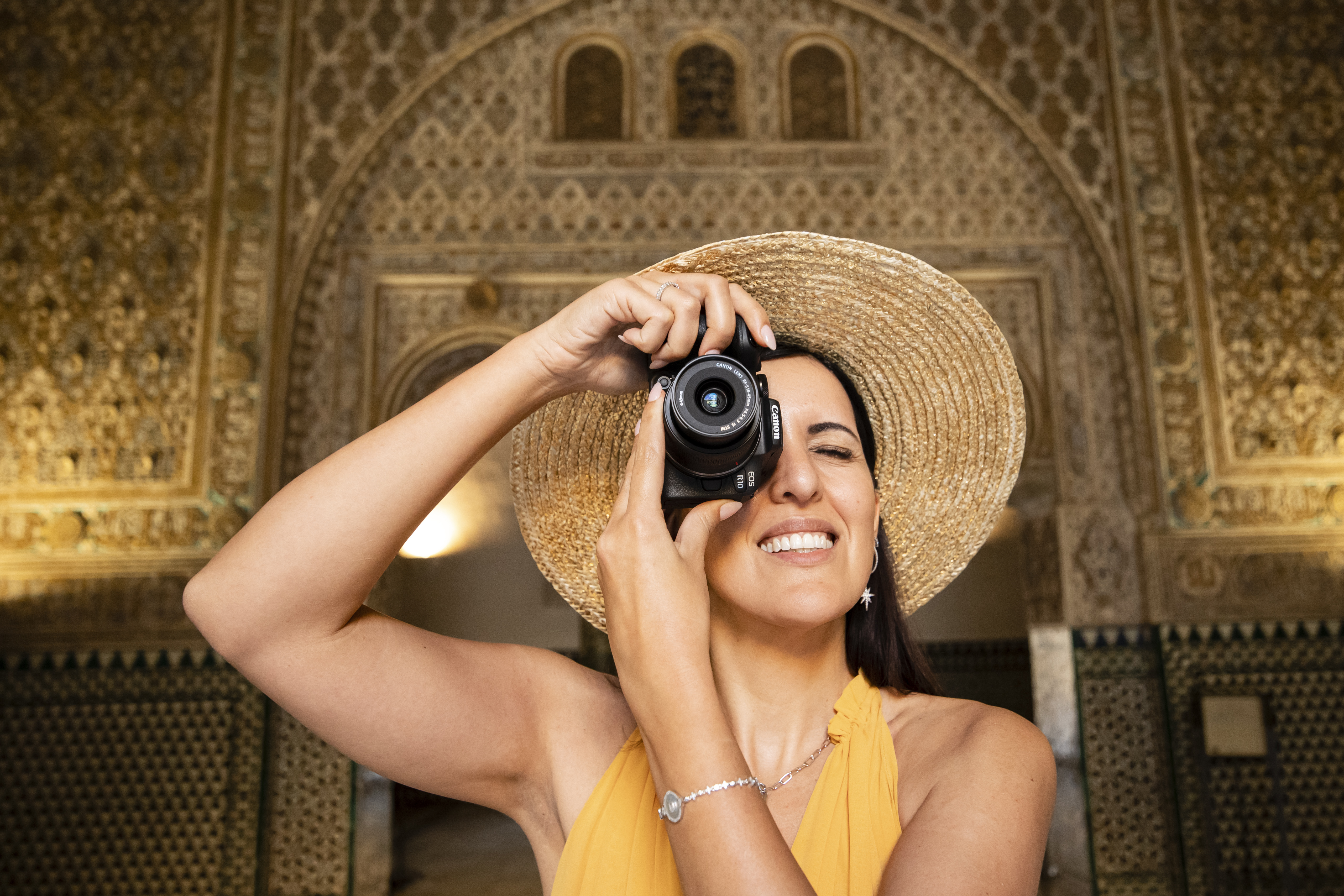 A person in a hat and a yellow dress holding a Canon EOS R10