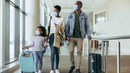 Photo of a masked family of three walking through an airport. 