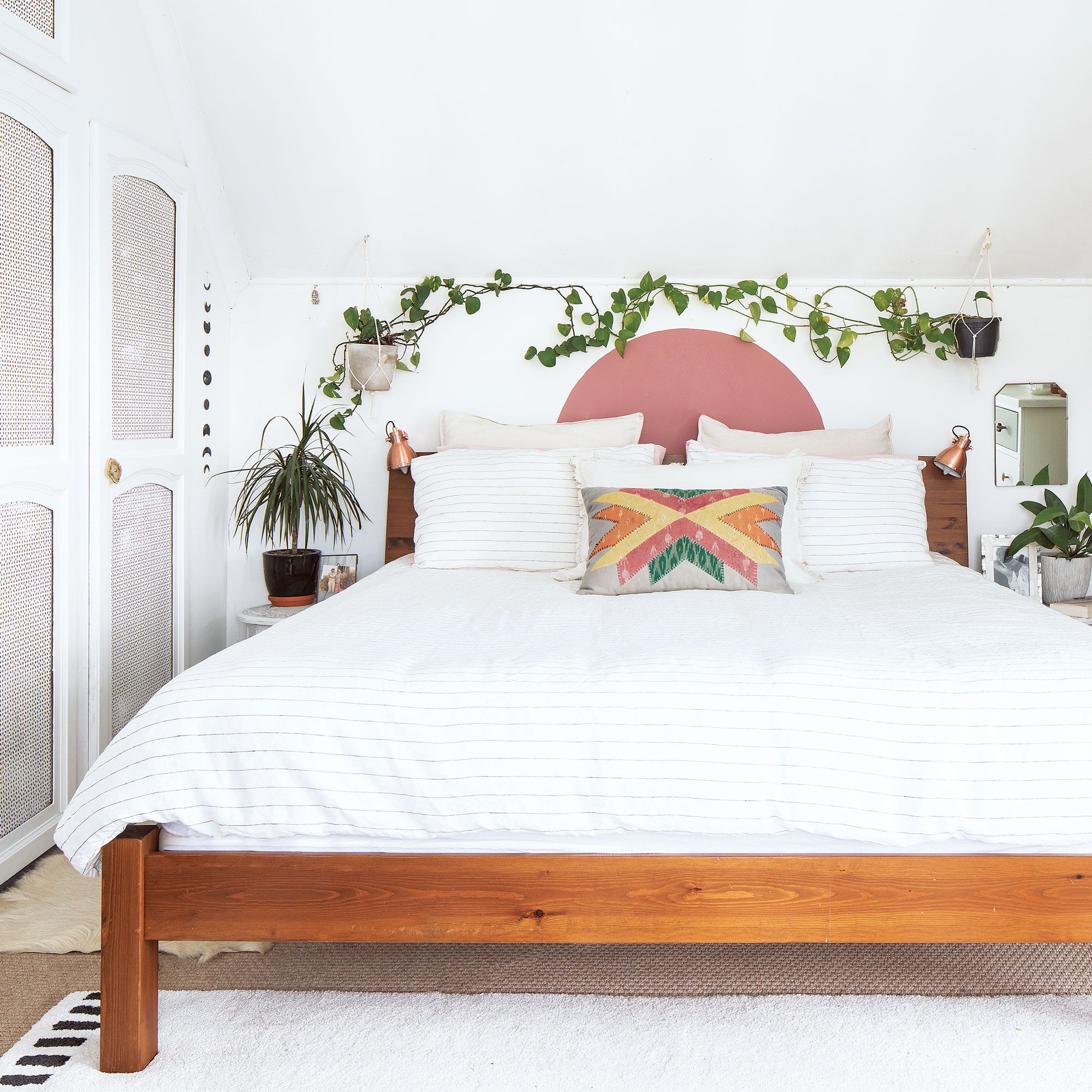 white boho bedroom with pink painted wall arch, plants and wooden bedframe