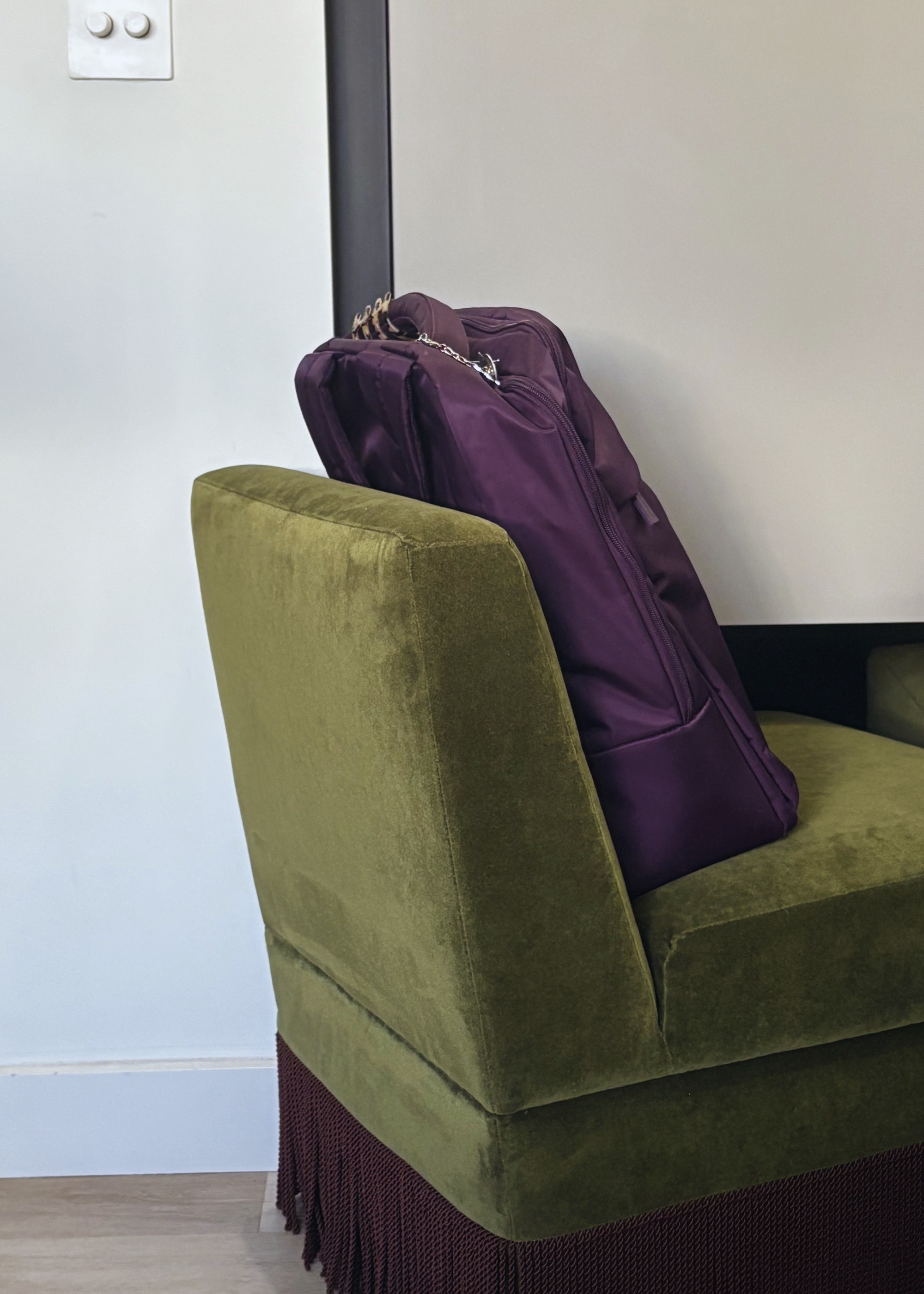 A purple Lipault backpack on a green art deco chair with a brown fringe